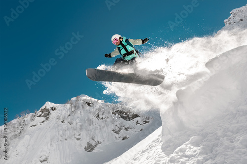 Billede på lærred Fast girl snowboarder jumps from springboard high in mountains