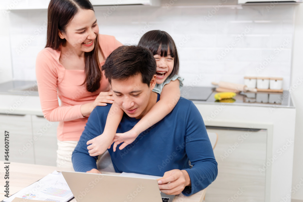 Work from home and concept family, beautiful Asian woman and Asian girl hugging her father's neck while working at home. Work from home and concept family, beautiful Asian woman and Asian girl hugging her father's neck while working at home.