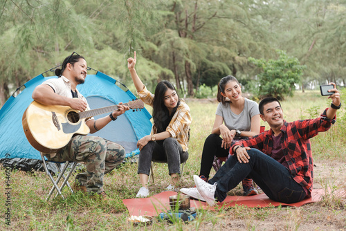 selfie together, a group of four asian men and women Camping and picnic in the forest, playing guitar and singing, outdoor activities concept.