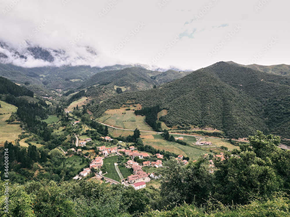 nice landscape of the small town at the bottom of the green valley between grass vegetation and forests next to the mountains a cloudy day, ruta del cares asturias, spain