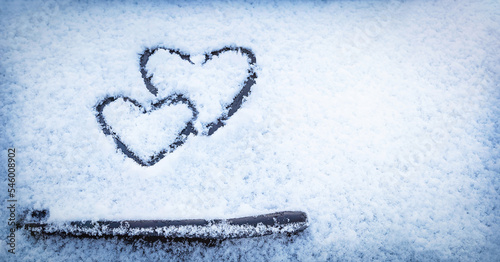 Two hearts (symbol of love) hand drawing (painted) on snow on the glass above windshield wiper of a car. Valentine's Day, love, winter, transport concept. Copy space. Selective focus.