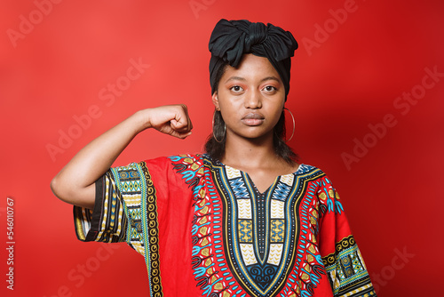 Black woman in typical African dress makes a feminist gesture with her arm while facing the camera