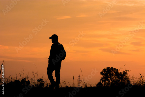 a silhouette of a person in a cap standing in tall grass, with a sunset in the background.