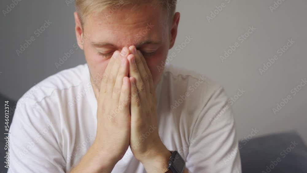 the man is very upset. he sits down on the couch and covers his face. the man is very upset. he sits down on the couch and covers his face.