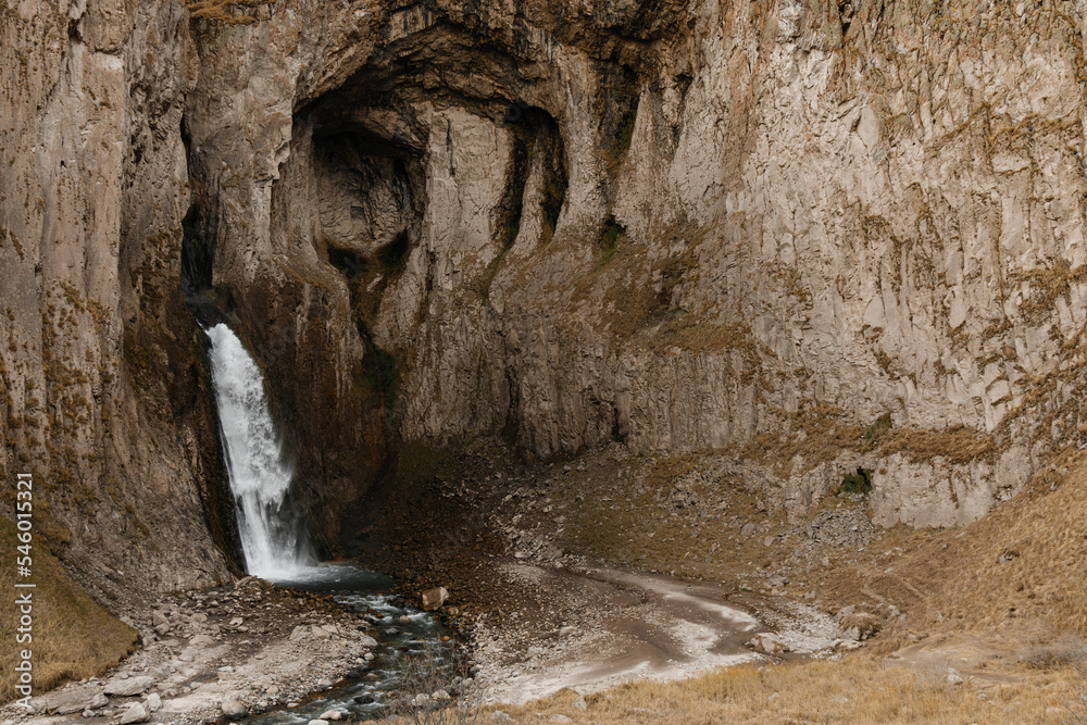 Obraz premium A high stormy waterfall flowing down in the massive rocks of Djily-su on an autumn day. Journey through the mountain beauties of the Caucasus 