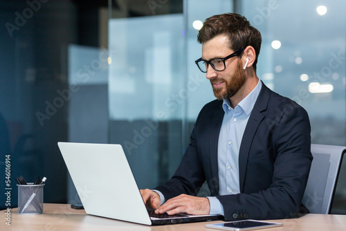 Successful mature businessman at work with laptop inside office, man in business suit sitting at desk typing on computer, satisfied with achievement result and work.