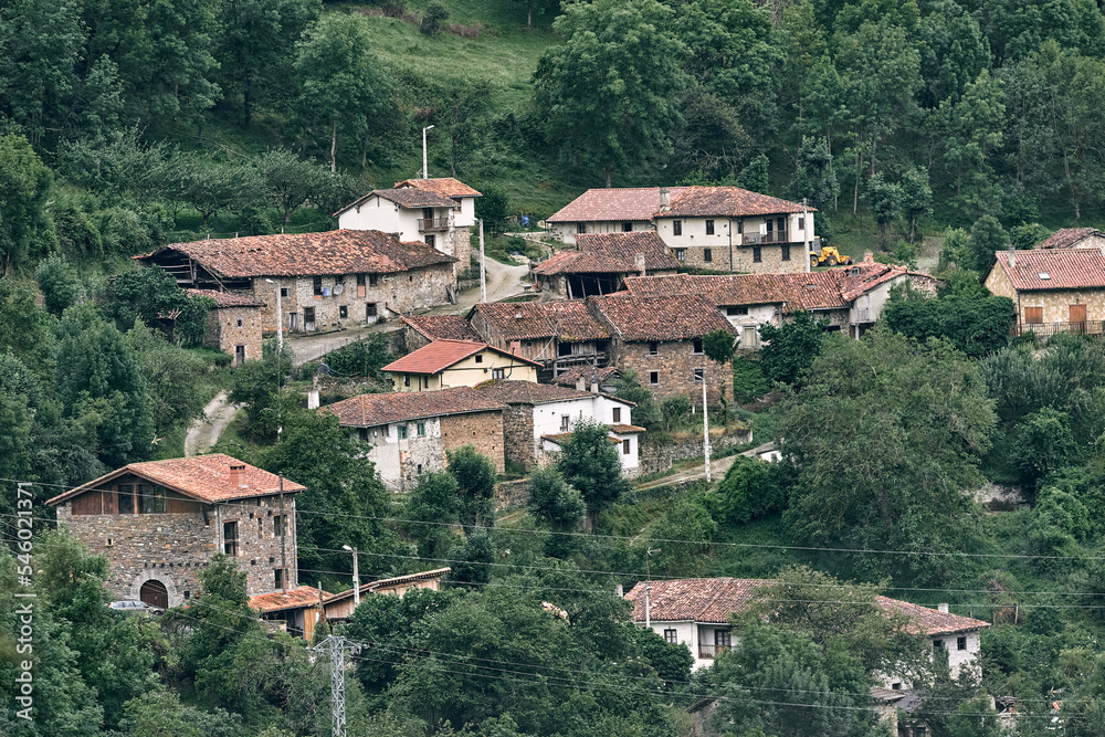 small quiet village with old stone houses and brown roofs in the middle of the road next to the forest, ruta del cares asturias, spain