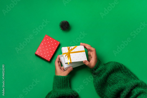 An ajar gift box in female hands over the table, gift boxes lie nearby, a Christmas tree, green background