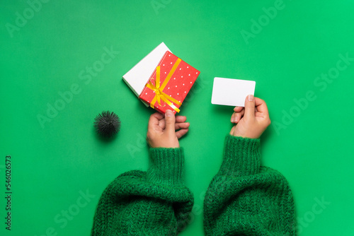 Female hands hold a gift kata and a red box with a golden ribbon on a green background