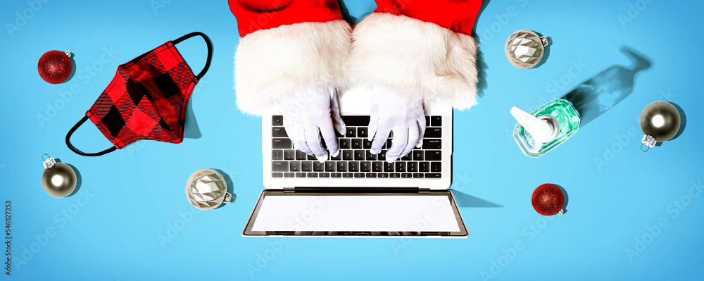 Santa Claus using a laptop computer with a mask and a sanitizer bottle from above