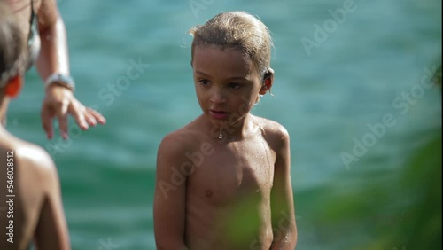 One pensive small boy standing outdoors. Wet child shivering outside shirtless after bathing at lake. Contemplative kid thinking outside in nature photo