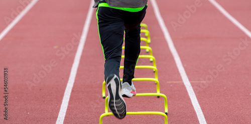 Rear view of a runner running over yellow mini hurdles on a track