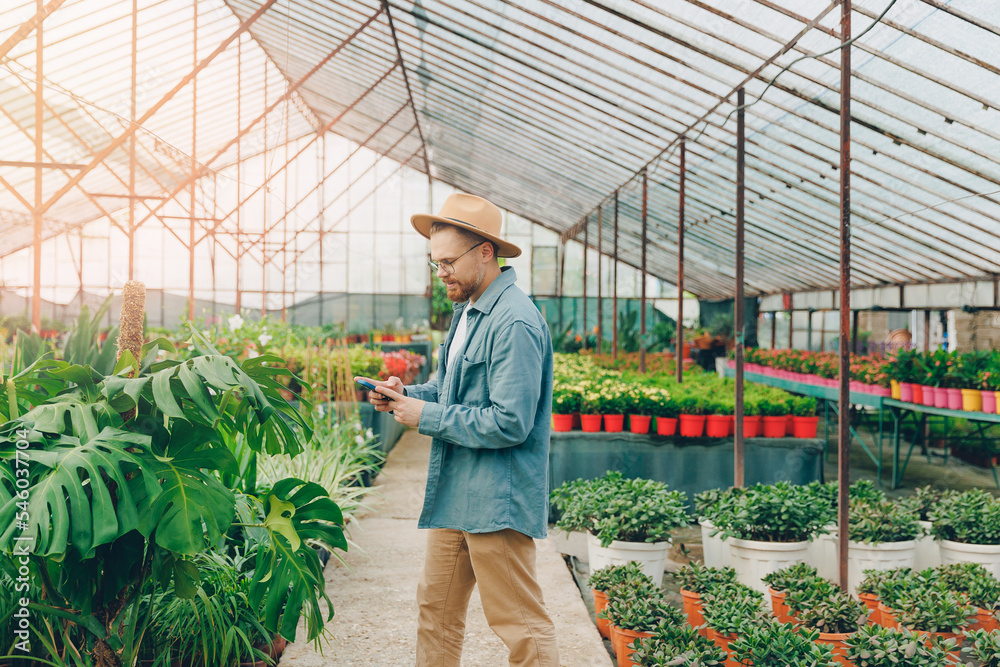 Smiling gardener young man talking on phone in greenhouse. Concept owner small business of sale flowers Smiling gardener young man talking on phone in greenhouse. Concept owner small business of sale flowers