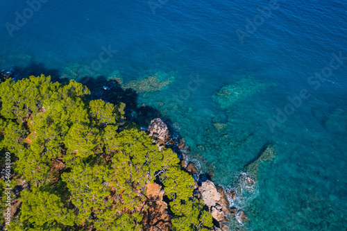 Aerial top view of clear blue water sea, rocks and forest at sunset in summer Turkey