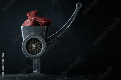 Making minced meat for beef meatballs in a manual meat grinder on a black background. Macro shot. Close up of metal meat grinder with raw meat photo