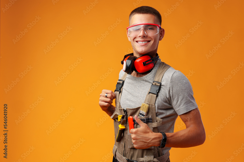 Young construction worker in uniform posing on yellow background in studio Young construction worker in uniform posing on yellow background in studio