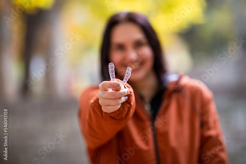 Happy young woman smiling with invisible teeth aligner during fall season at park.