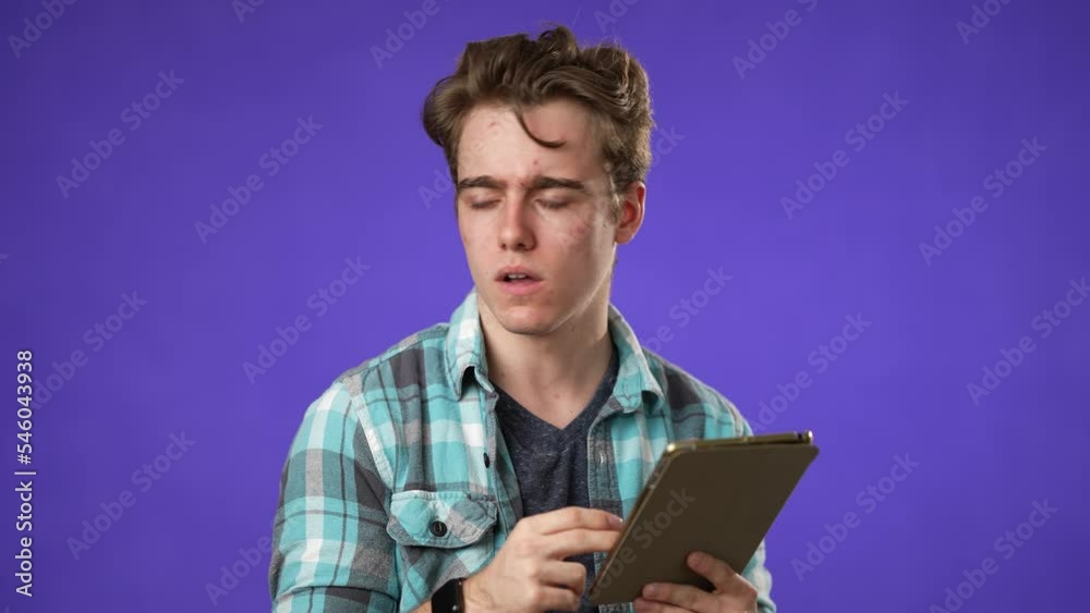 Portrait of happy smiling young guy 20s in shirt reading bad news on tablet computer isolated on purple background studio. Portrait of happy smiling young guy 20s in shirt reading bad news on tablet computer isolated on purple background studio.