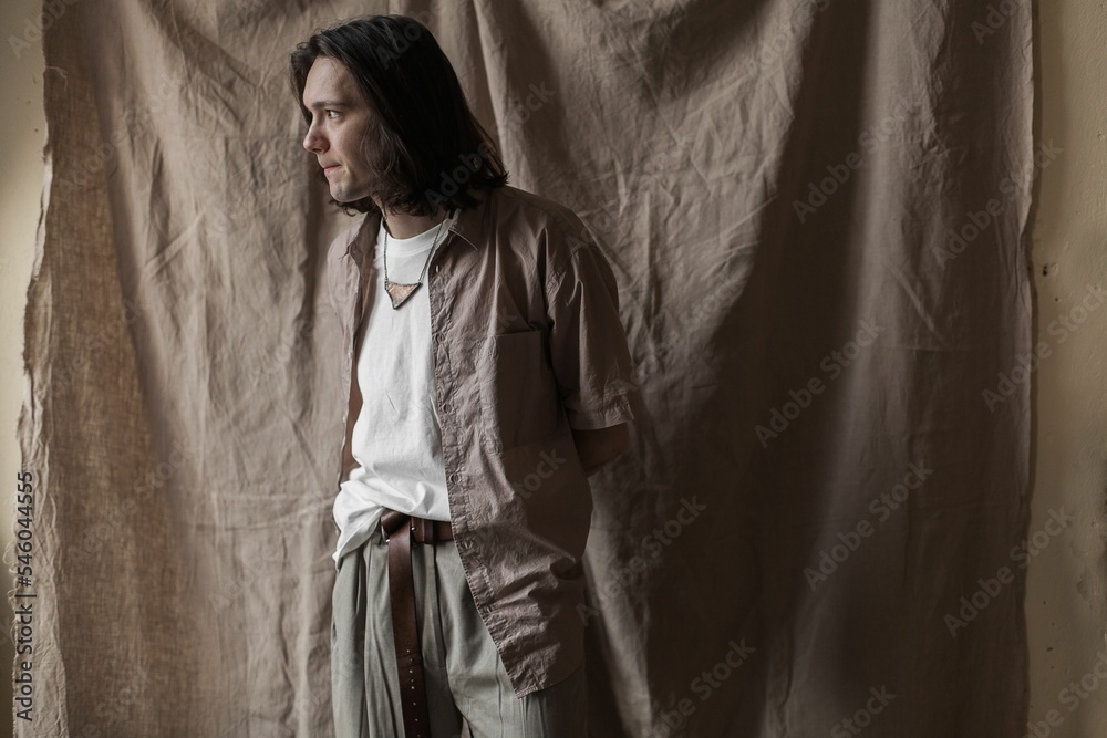 Naklejka premium Aesthetic shot of a handsome young man in silk clothing against a beige background