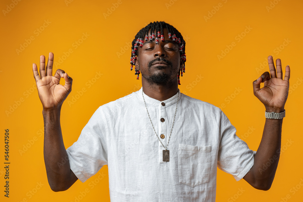 African man standing over isolated yellow background relax and doing meditation gesture with fingers African man standing over isolated yellow background relax and doing meditation gesture with fingers
