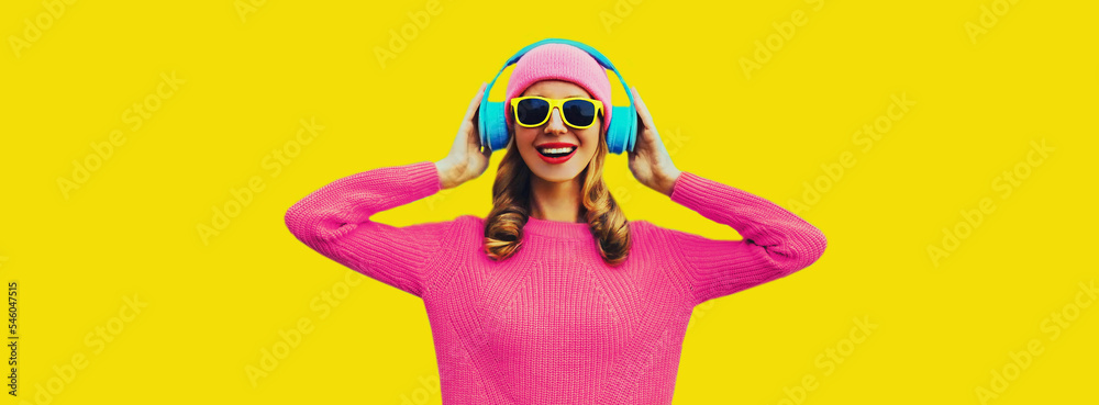 Portrait of happy smiling young woman with headphones listening to music wearing colorful pink sweater on yellow background Portrait of happy smiling young woman with headphones listening to music wearing colorful pink sweater on yellow background