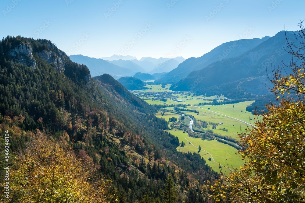 Aerial view of a river in a green meadow surrounded by high mountains on a sunny day