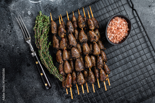 Grilled shish kebab with chicken hearts on a grill. Black background. Top view