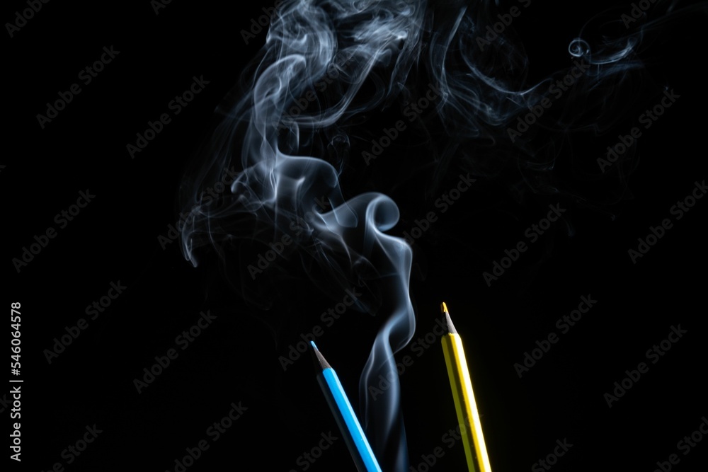 A yellow and a blue colored pencil touching the white smoke comi A yellow and a blue colored pencil touching the white smoke comi