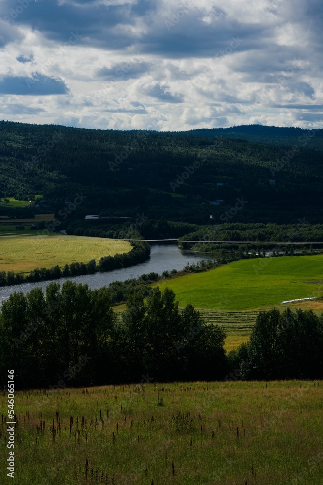 Vertical shot of a beautiful landscape with green fields, hills, and a river in Selbu, Norway
