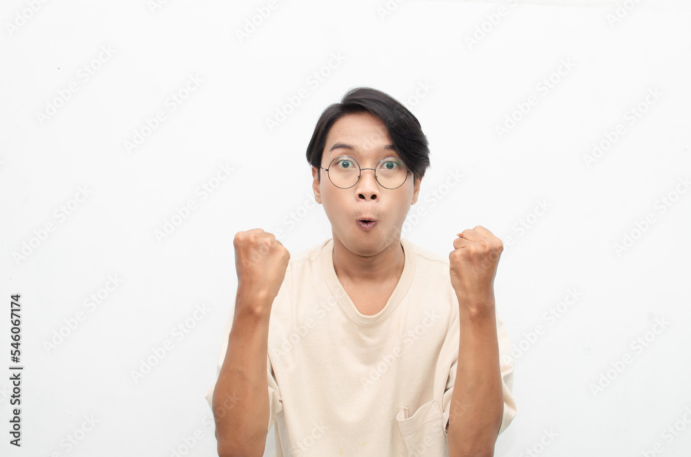 Asian young man wearing casual beige tshirt surprised, amazed, wow shocked raising arms gesturing victory and yes gesture Asian young man wearing casual beige tshirt surprised, amazed, wow shocked raising arms gesturing victory and yes gesture