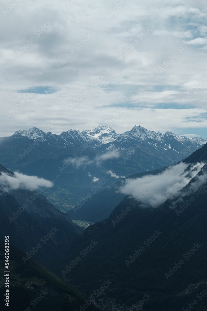 Vertical aerial view of snowcap Alpine summits under white clouds in the sky