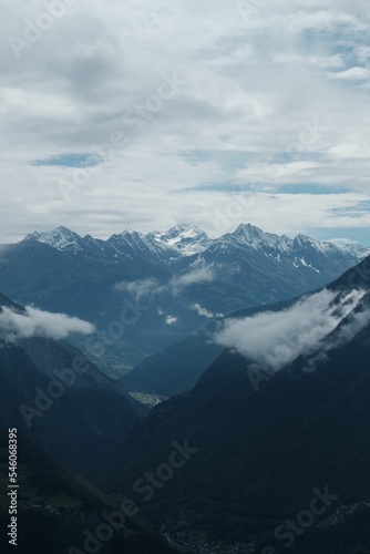 Vertical aerial view of snowcap Alpine summits under white clouds in the sky
