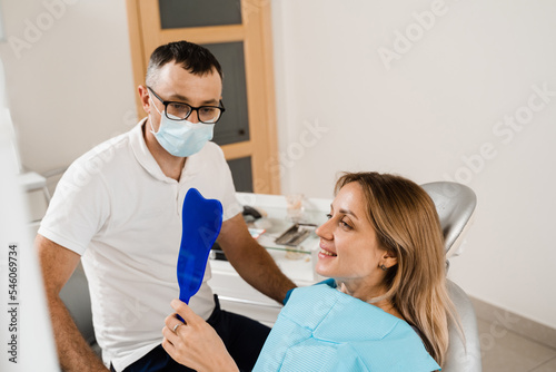 Dentist and woman patient in dentistry. Consultation with dentist at dentistry. Teeth treatment. Girl looking in the mirror at the dentist. Happy patient of dentistry.