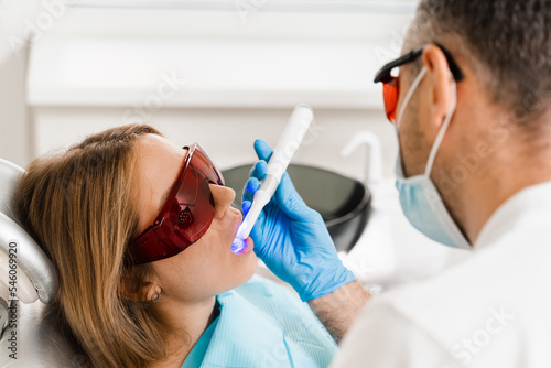 Uv illumination of photopolymer tooth filling procedure. Dentist in red protective glasses treats and removes caries in woman patient.