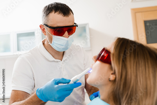 Uv illumination of photopolymer tooth filling for woman in dentistry. Dentist in red protective glasses treats and removes caries of girl patient.