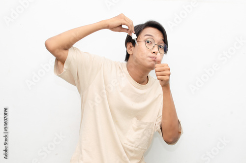 asian young man in casual beige tshirt applying beauty acne serum using pipette and smiling at camera isolated over red background