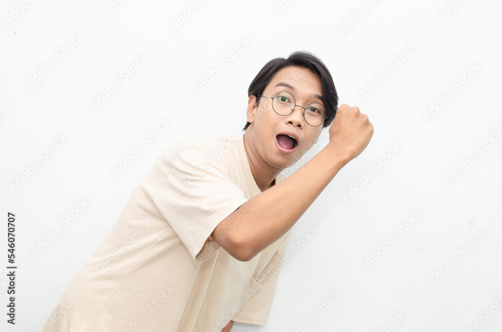 Asian young man wearing casual beige tshirt surprised, amazed, wow shocked raising arms gesturing victory and yes gesture Asian young man wearing casual beige tshirt surprised, amazed, wow shocked raising arms gesturing victory and yes gesture