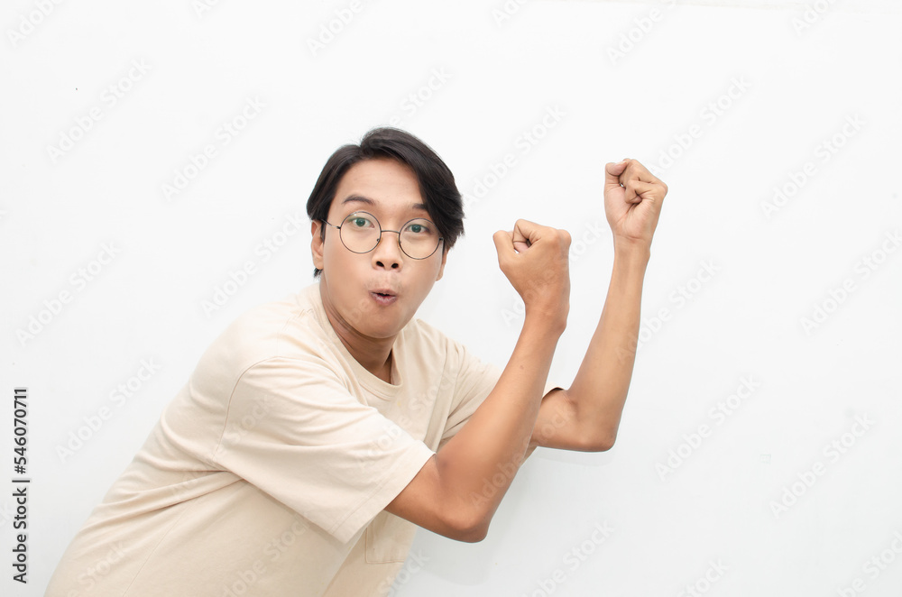 Asian young man wearing casual beige tshirt surprised, amazed, wow shocked raising arms gesturing victory and yes gesture Asian young man wearing casual beige tshirt surprised, amazed, wow shocked raising arms gesturing victory and yes gesture