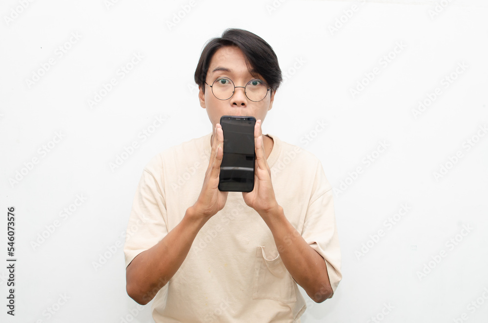 excited young asian man in beige tshirt holding and showing phone screen with happy euphoric shocked wow expression. man pointing to screen phone with thumb up. billboard model advertisment concept. excited young asian man in beige tshirt holding and showing phone screen with happy euphoric shocked wow expression. man pointing to screen phone with thumb up. billboard model advertisment concept.
