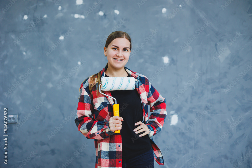 A beautiful young woman in a checkered shirt is renovating her room, holding a paint roller A beautiful young woman in a checkered shirt is renovating her room, holding a paint roller