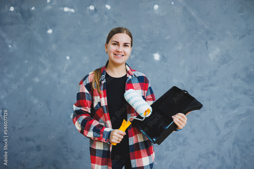 A beautiful young woman in a checkered shirt is renovating her room, holding a paint roller A beautiful young woman in a checkered shirt is renovating her room, holding a paint roller