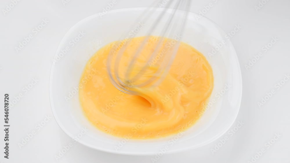 Stirring eggs with whisk in white plate, macro shot. Cooking omelette Stirring eggs with whisk in white plate, macro shot. Cooking omelette