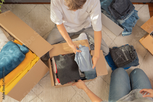 Woman and child sorting clothes and packing into cardboard box. Donations for charity, help low income families, declutter home, sell online, moving moving into new home, recycling, sustainable living