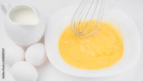 Stirring eggs with whisk. Сhef whisking eggs in white bowl, cooking omelette with milk