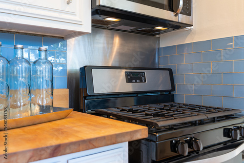 Kitchen detail of stove with butcher block counter  blue tile backsplash and three glass bottles.