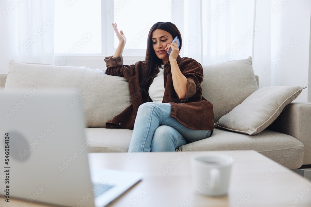 Woman blogger with phone lying at home and talking on the phone on sofa with laptop and working freelancer online, smiling with teeth Woman blogger with phone lying at home and talking on the phone on sofa with laptop and working freelancer online, smiling with teeth