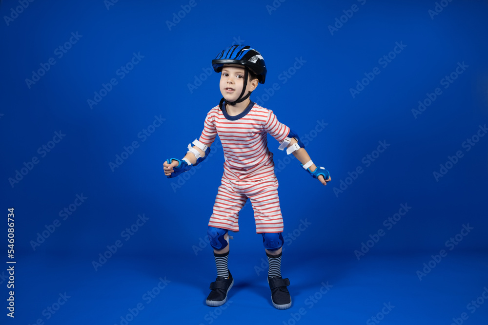 A happy boy in a protective helmet, elbow pads and gloves on a blue background. Protection when riding a bicycle, skateboard, roller skate