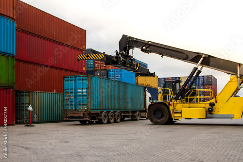 Truck while loading in logistic shipping yard with cargo container. Forklift truck handling truck. Logistic import export concept. Loading and unloading of containers in the port.