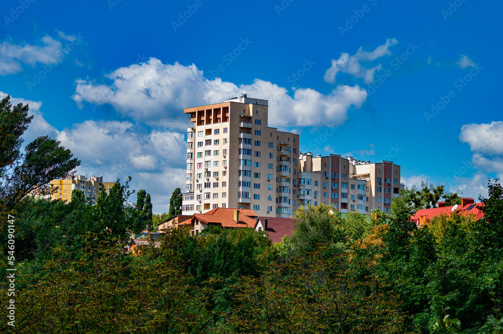 Multi-storey residential building on the city skyline against the blue sky. Residential building. Apartment in a multi-storey building. City real estate. The beauty. Business. White clouds.
