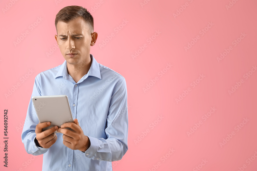 Thoughtful young man with tablet computer on pink background Thoughtful young man with tablet computer on pink background